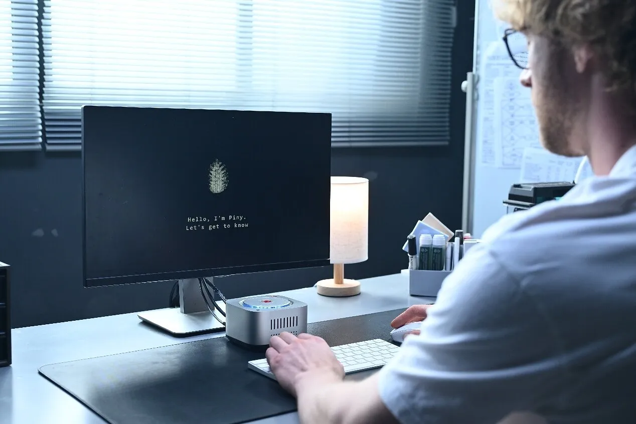 Man at a desk using a computer displaying a fingerprint and greeting beside a small device.