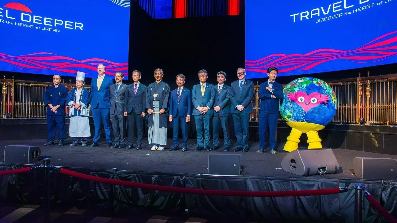 A group of people on a stage beneath Travel Deeper Japan screens, beside a colourful globe mascot.