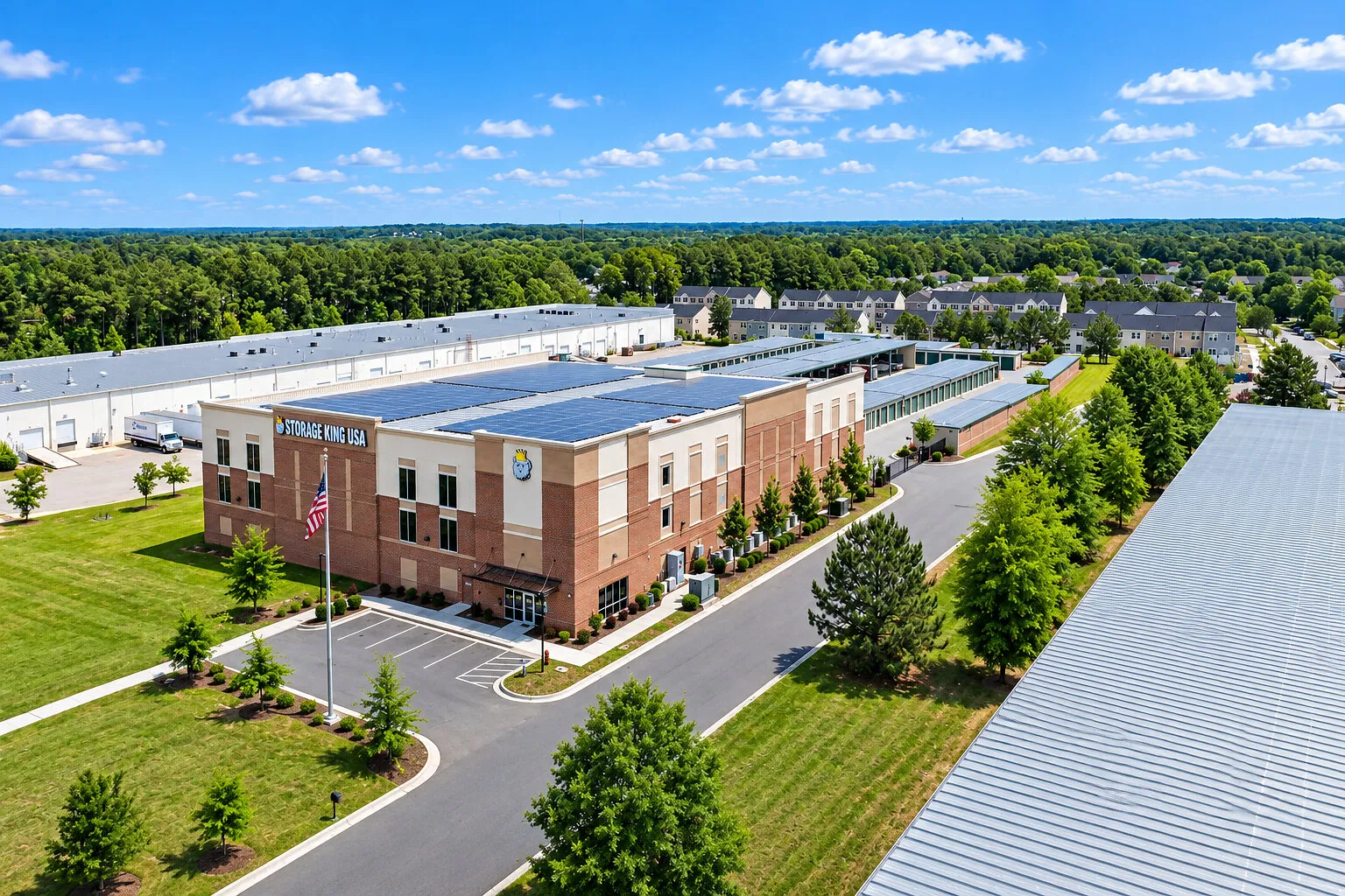 Aerial view of a brick commercial building with solar panels, parking spaces and surrounding trees.