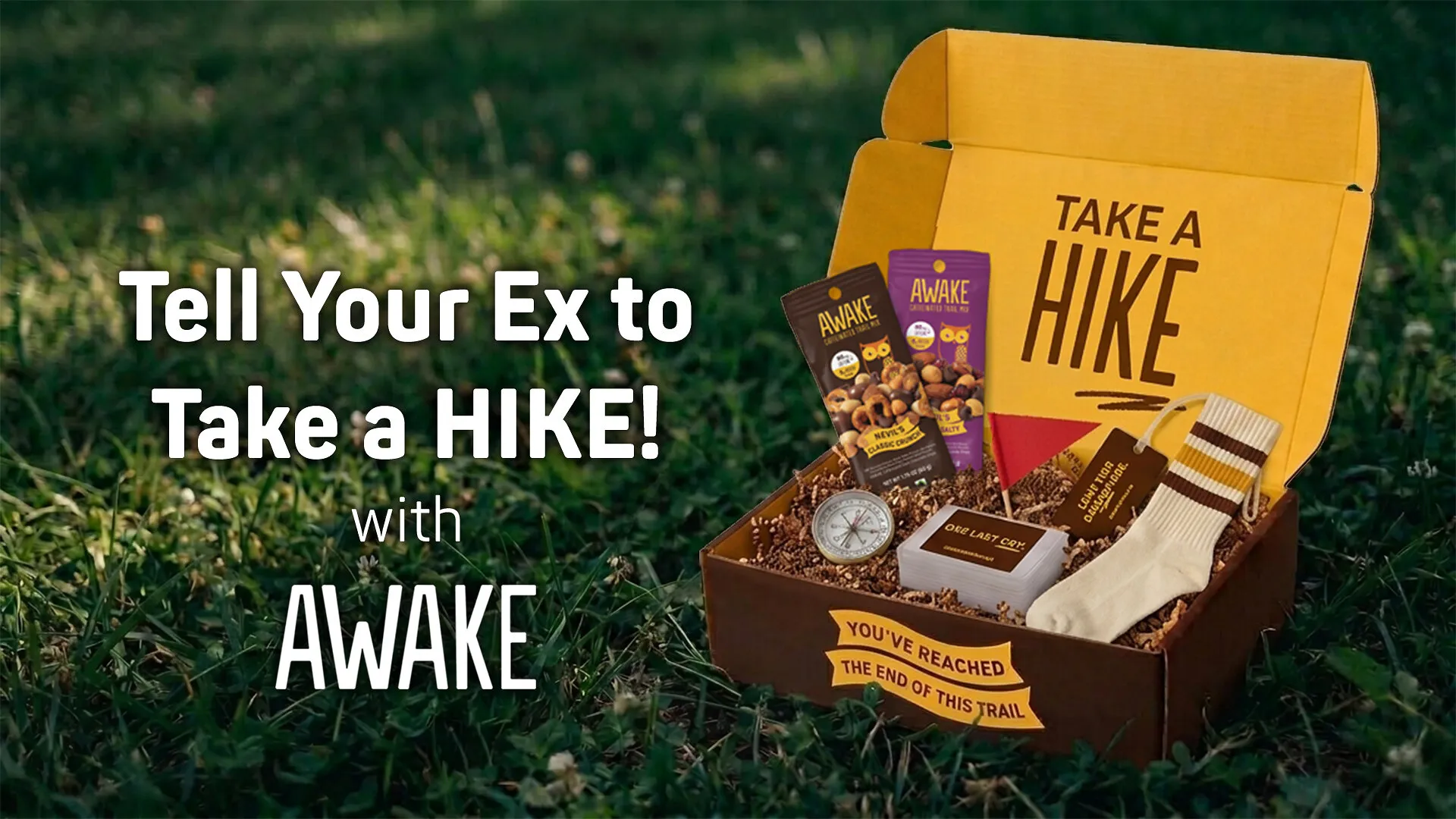Open gift box with AWAKE snacks, socks, compass and cards on grass beside “Tell Your Ex to Take a Hike” text