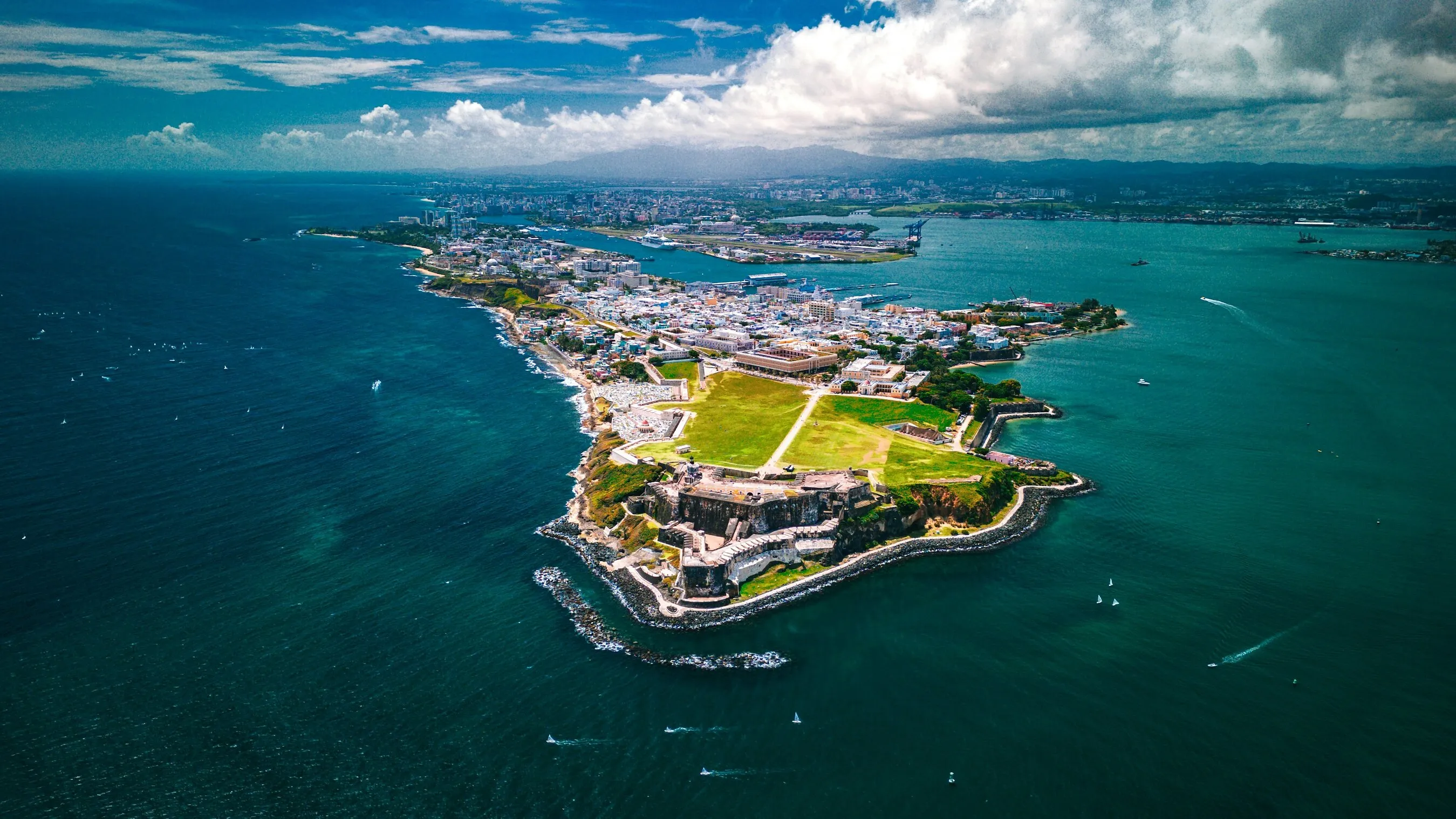 Aerial view of a coastal fort, green lawn and city surrounded by turquoise water in Puerto Rico