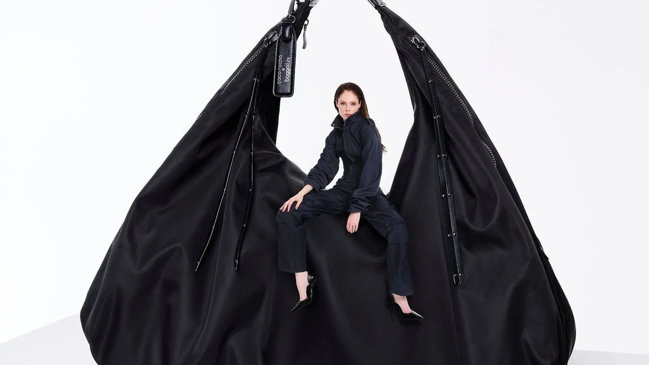 Woman in black seated inside an oversized black zippered bag.