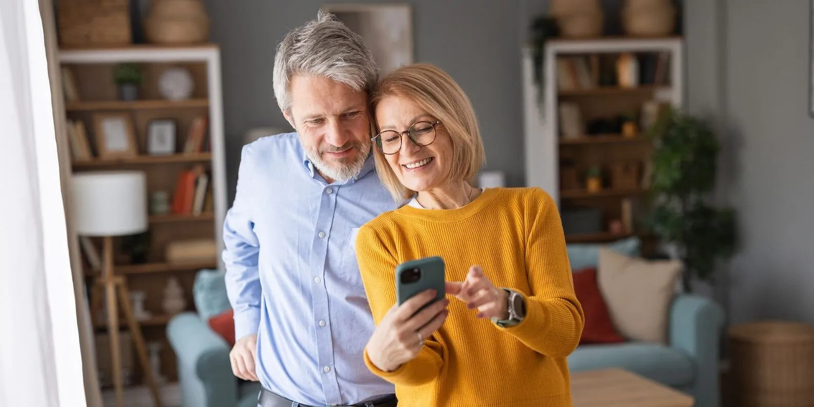 Smiling older couple looking at a smartphone in a living room.