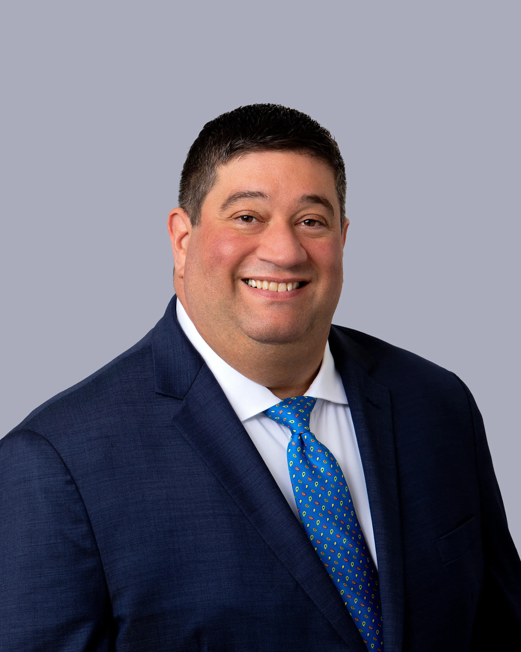 Brian Botkin in a navy suit and patterned blue tie against a gray background.