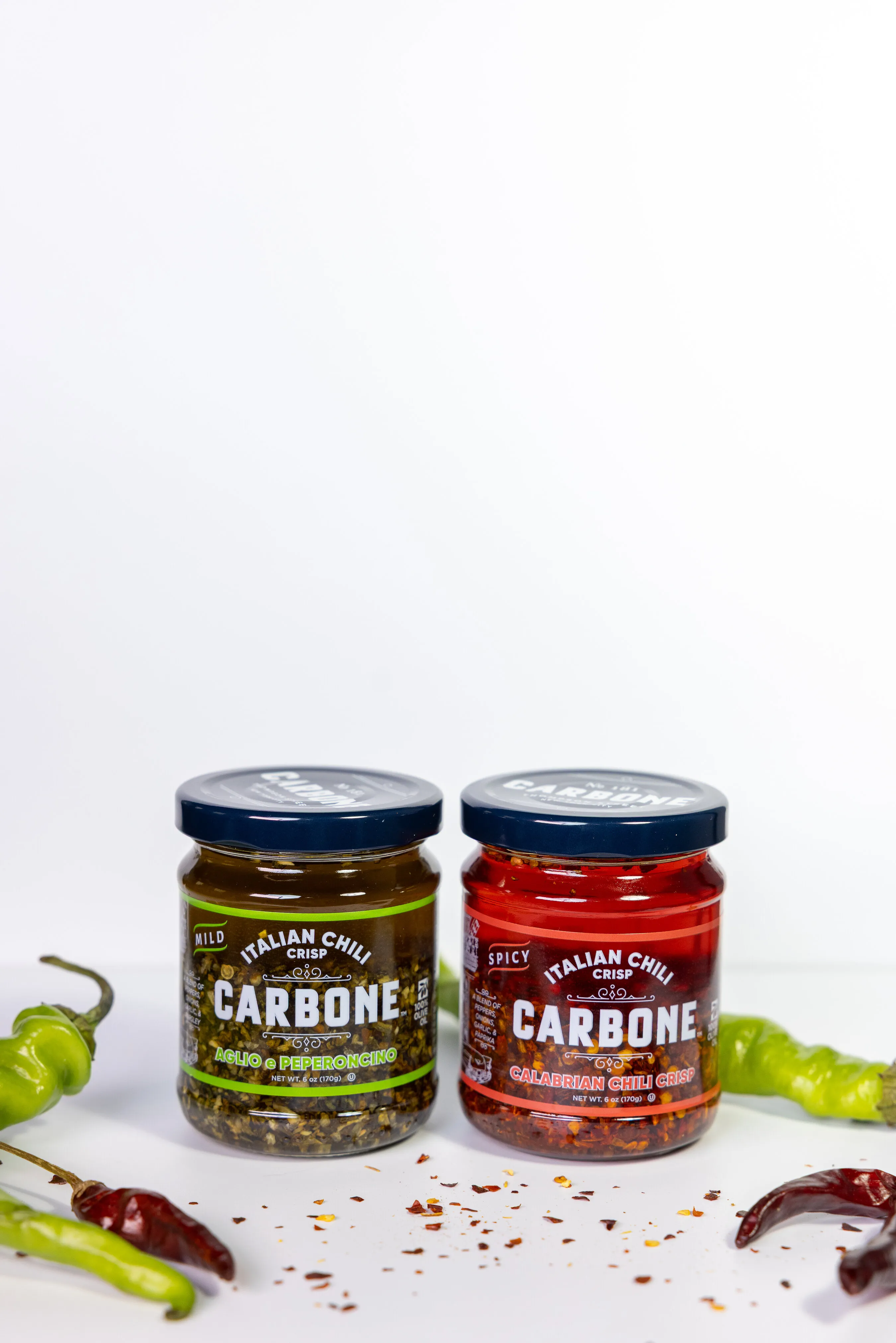 Two jars of Carbone Italian chili crisp, mild and spicy, with green and red peppers.