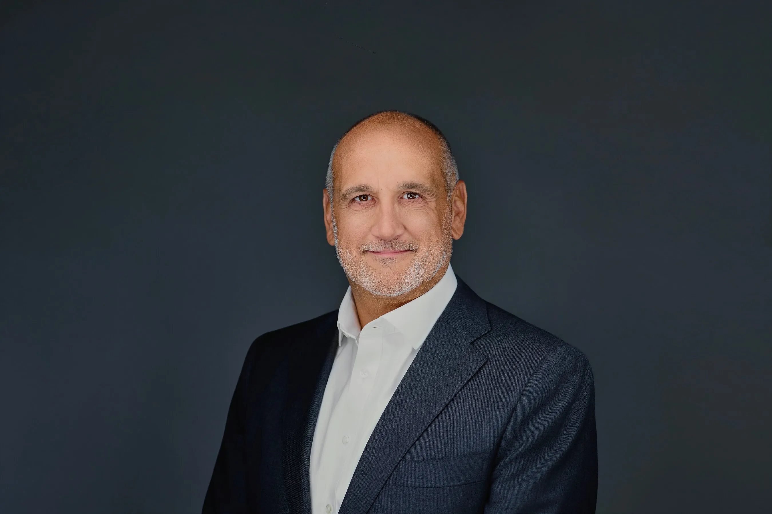Chris Valpone in a dark suit jacket and white shirt against a dark background.