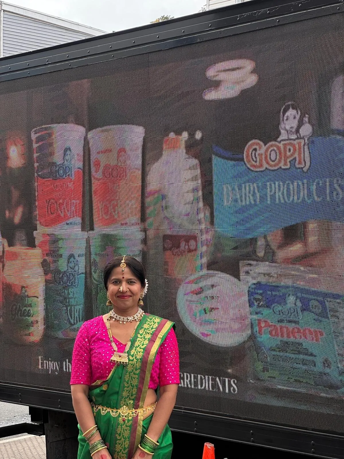Archana Chandra in a green and pink sari stands before the Diwali Celebration LED truck.
