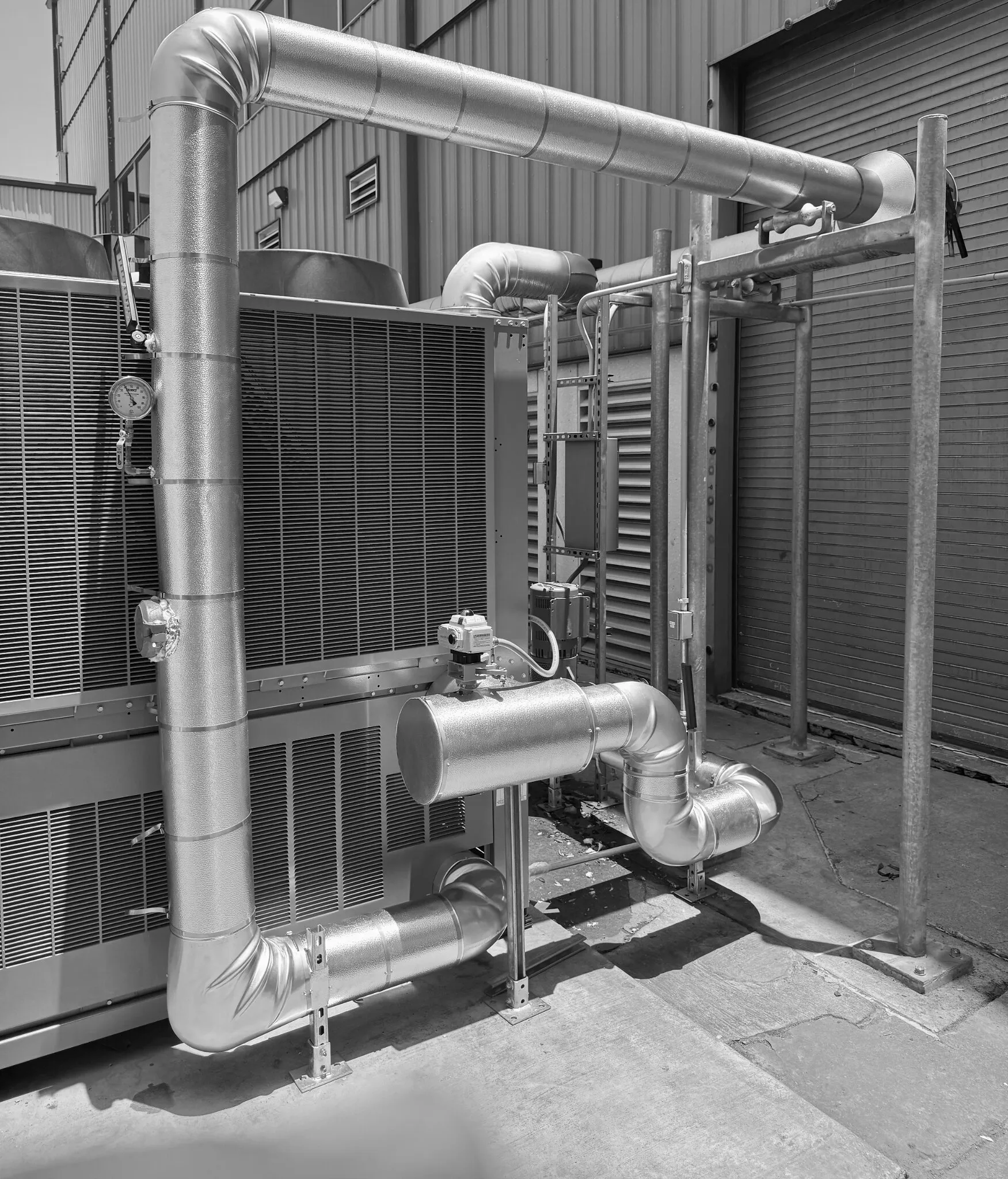 Insulated metal piping connected to an outdoor industrial cooling unit beside a building wall