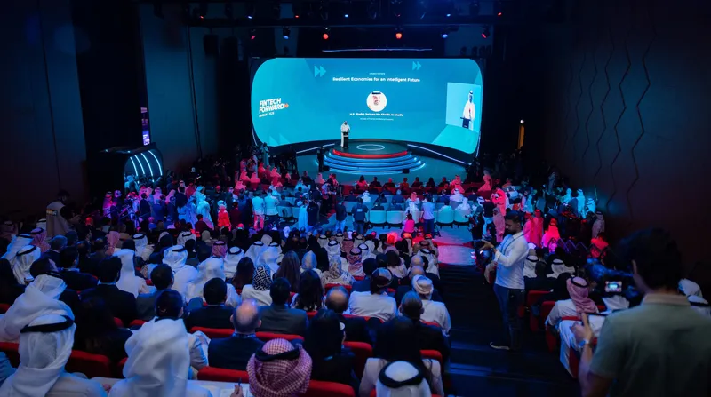 Audience seated at a conference facing a presenter on a blue-lit stage