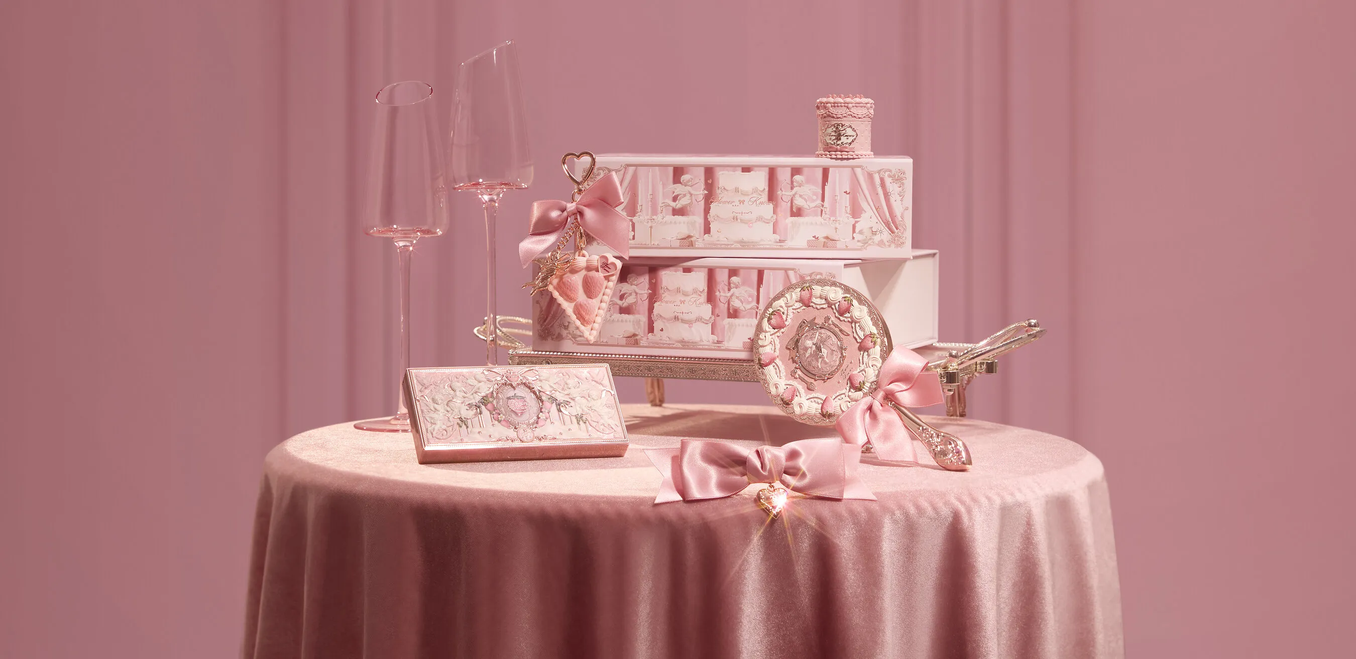 Pink gift boxes, champagne glasses and ornate heart-themed accessories on a satin-covered table.
