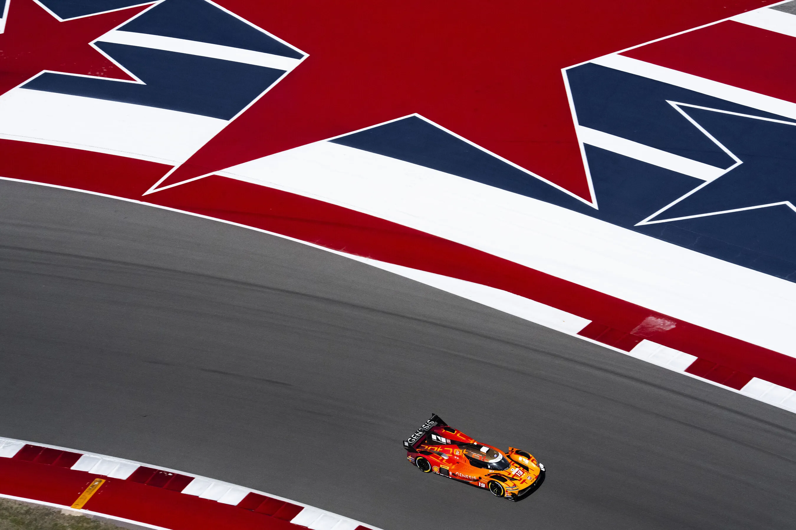 Orange Genesis race car on a track beside red, white and blue painted runoff.