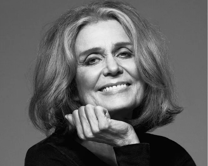 Black-and-white close-up portrait of a smiling woman resting her chin on her hand.