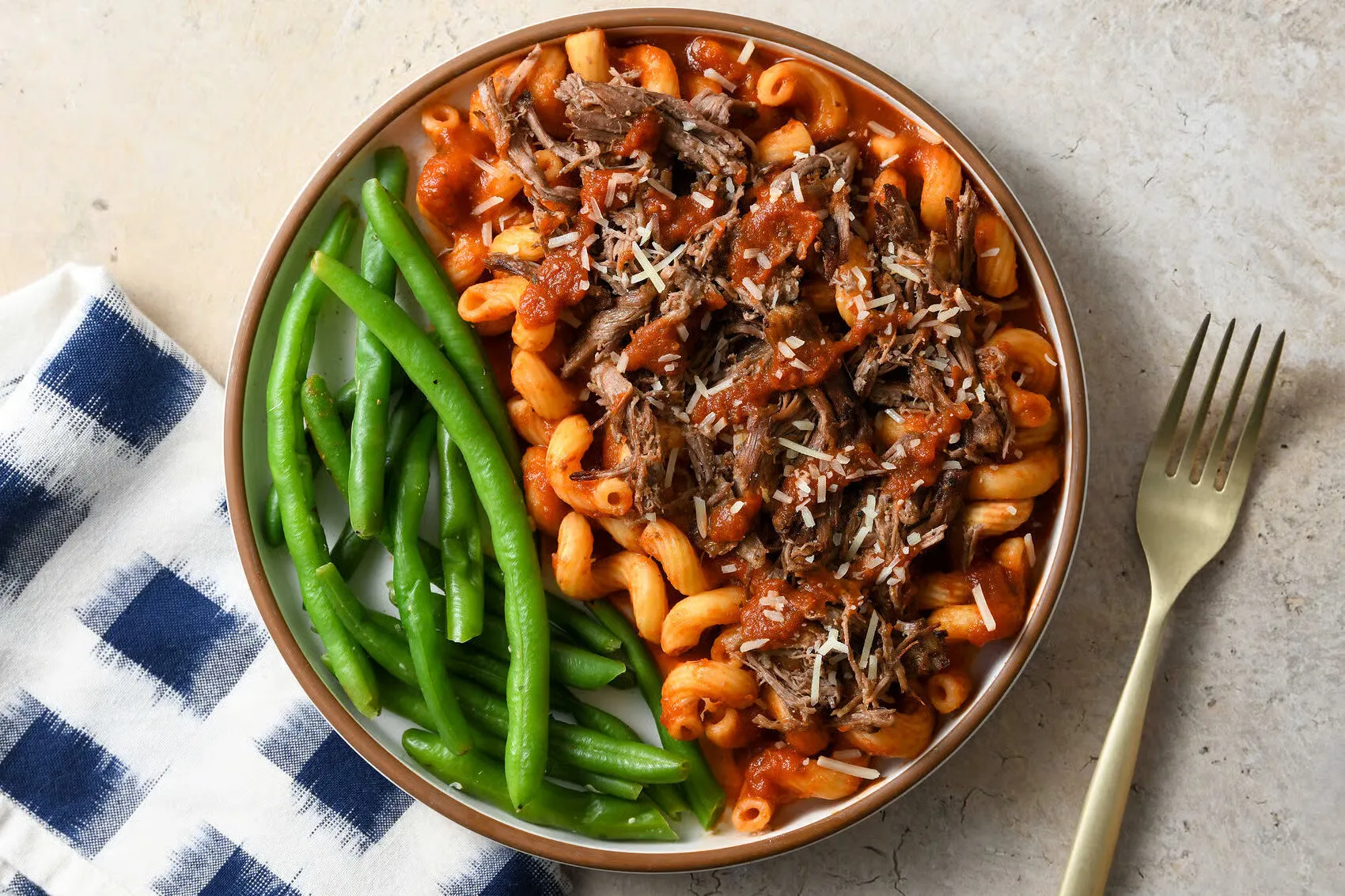 Braised beef tomato ragu pasta with green beans, Parmesan, a napkin, and a fork.