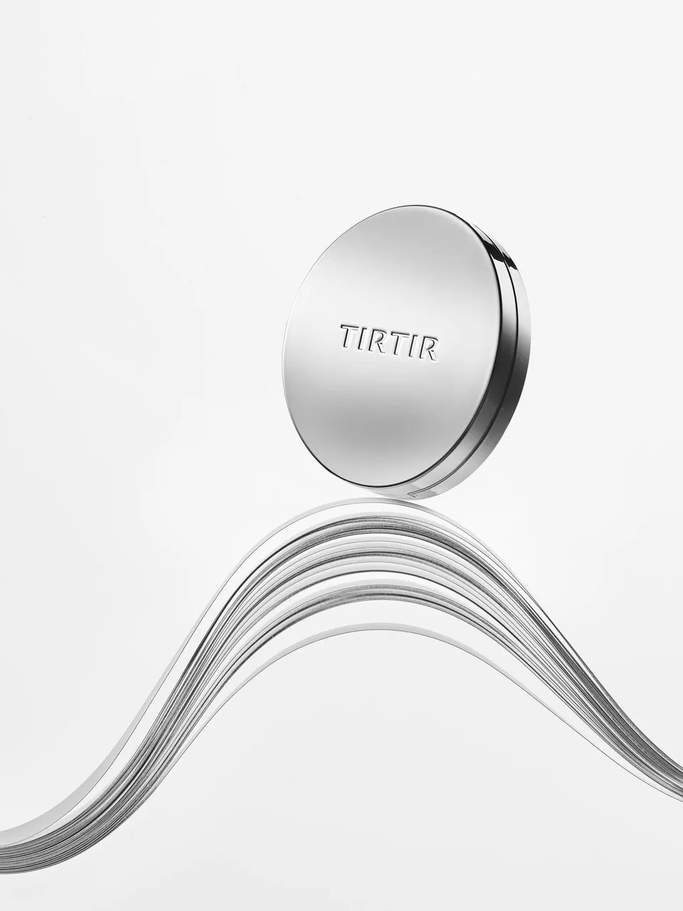 A silver TIRTIR compact floating above layered metallic waves.