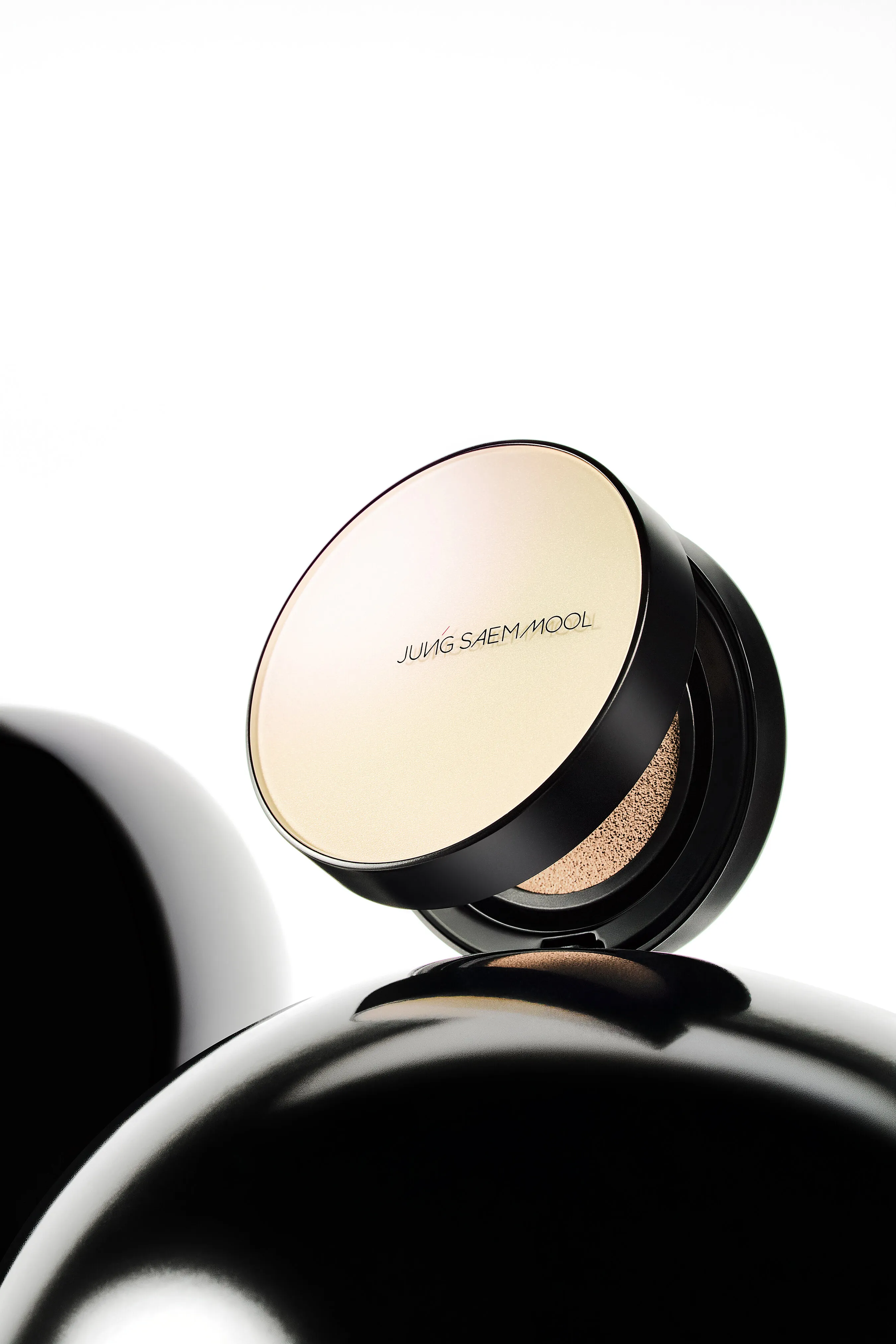 Open black cushion compact with beige makeup and a gold lid on a white background