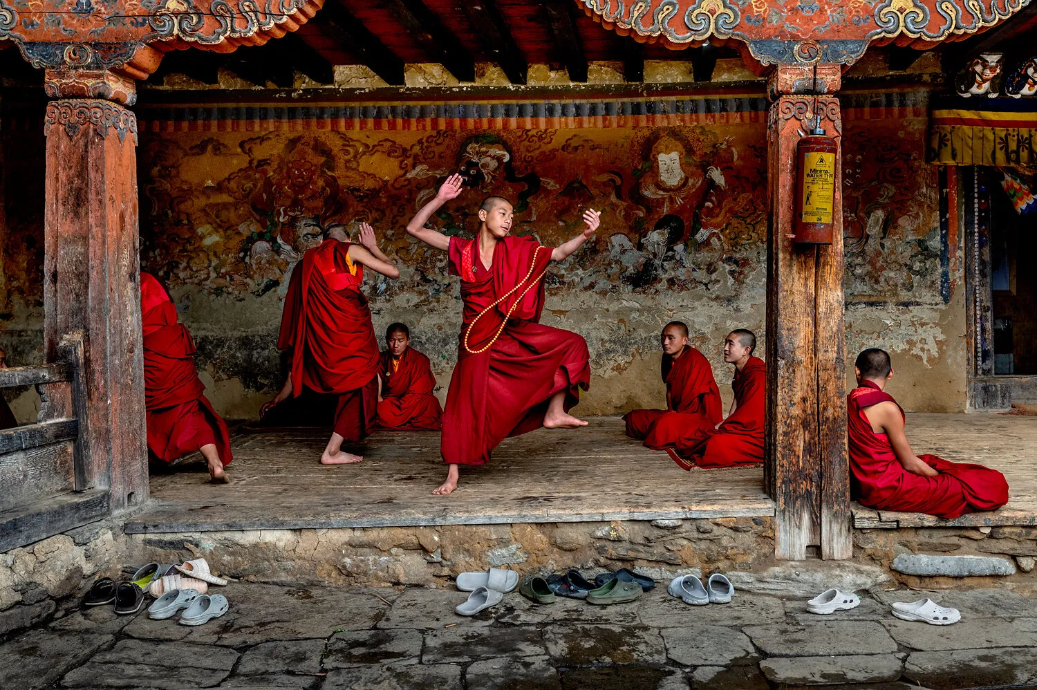 Monks in red robes practice martial arts inside a temple, with sandals lined outside.