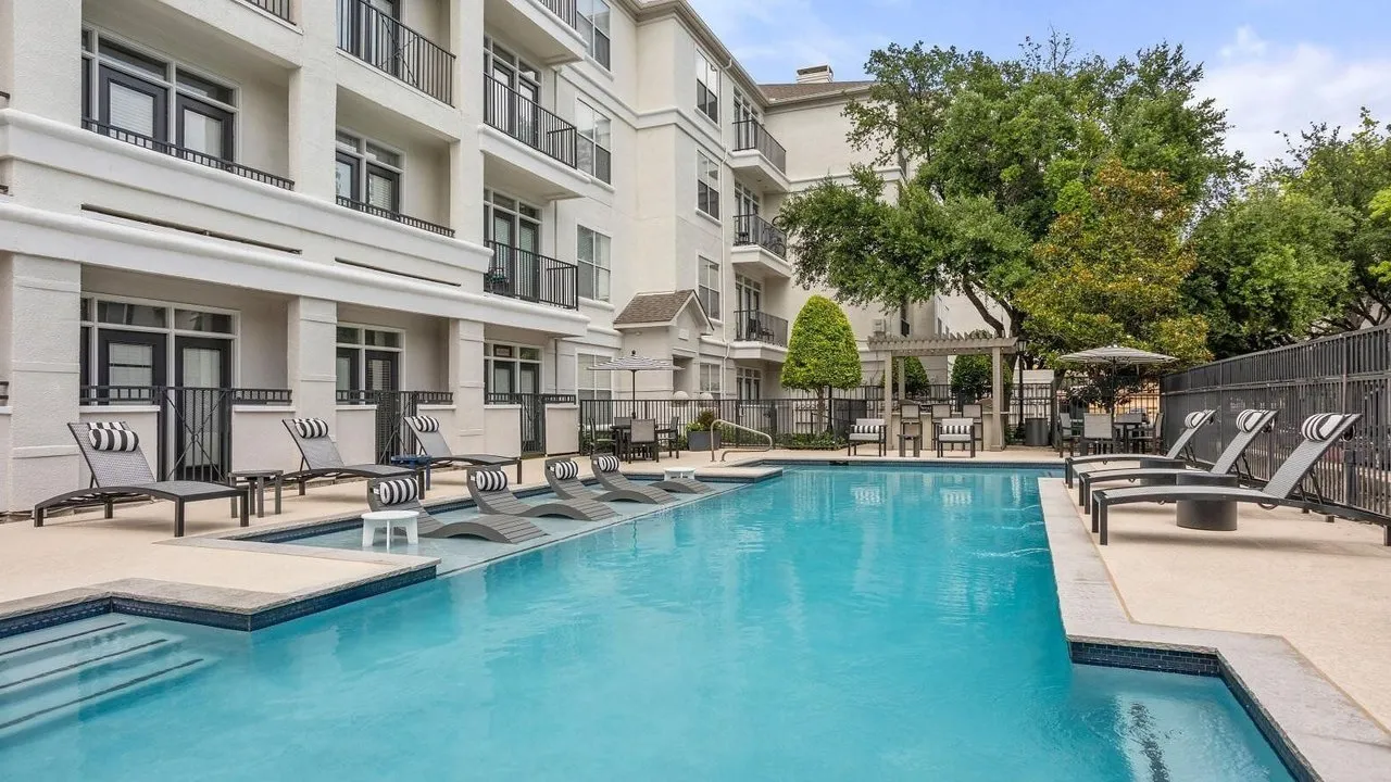 Outdoor swimming pool with striped lounge chairs beside a white apartment building and trees