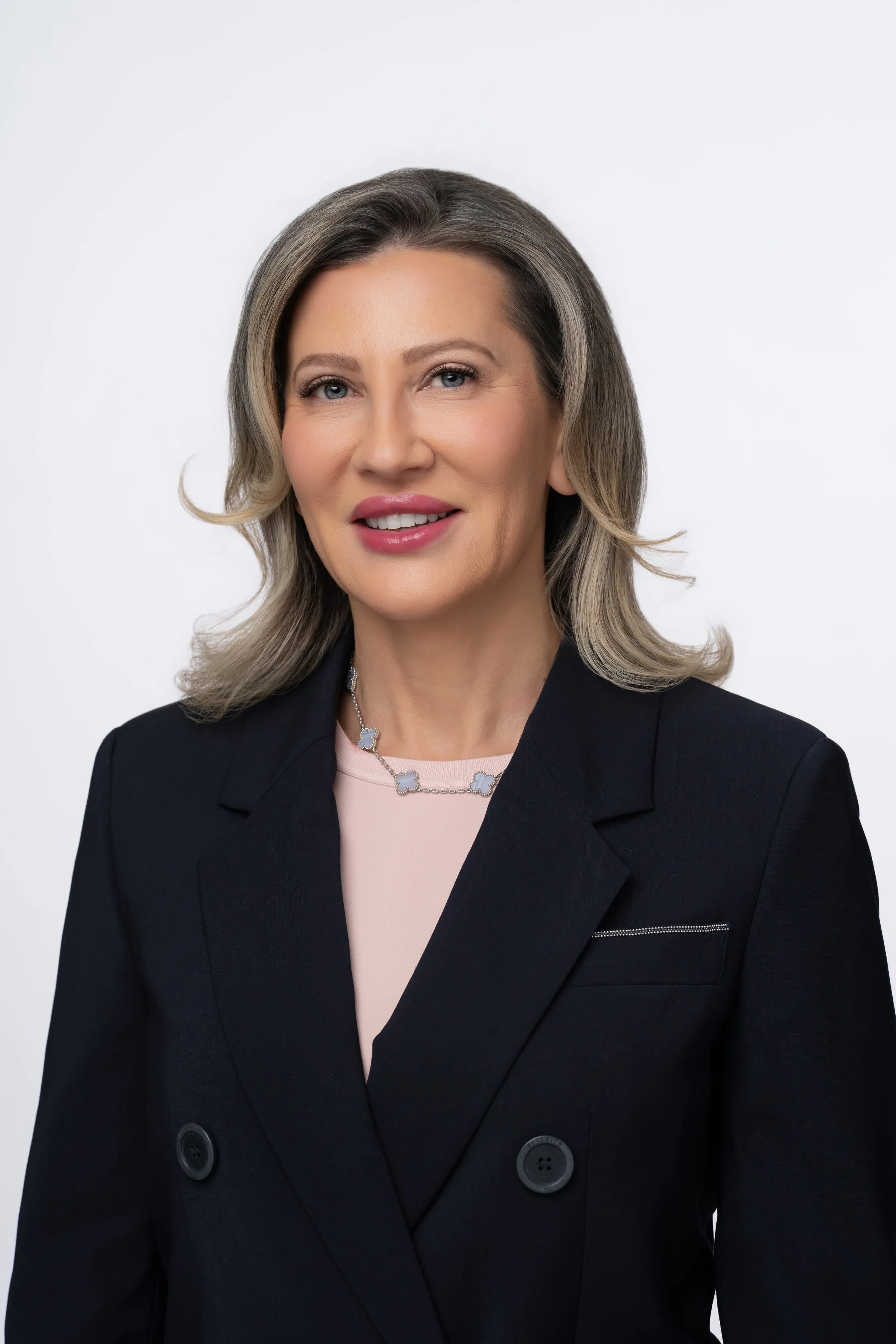A woman in a dark blazer and pink top against a light background