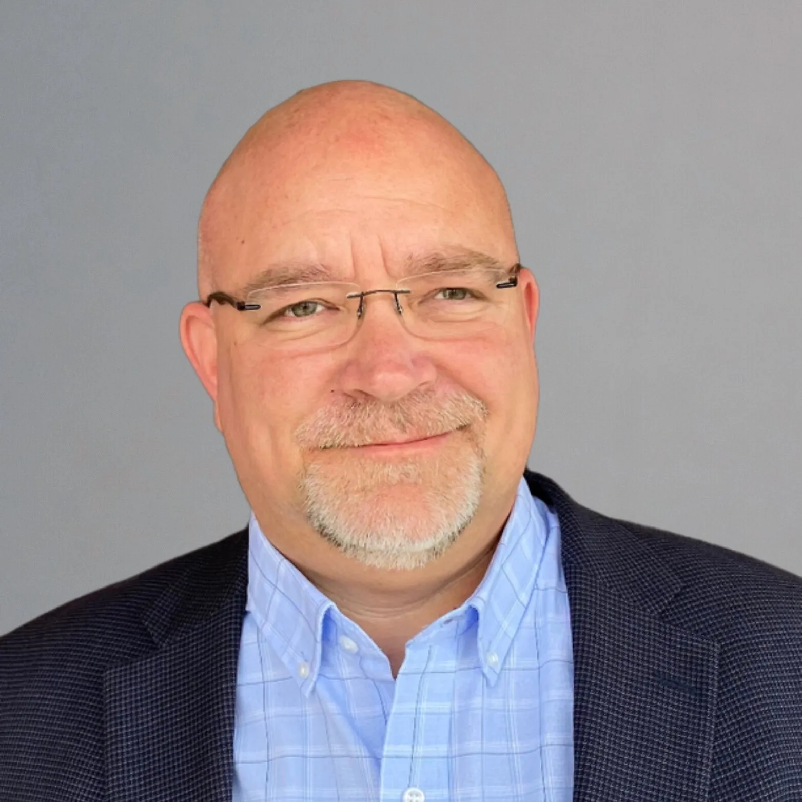 Mike Jones, President of Global Operations, wearing glasses and a blazer against a gray background.
