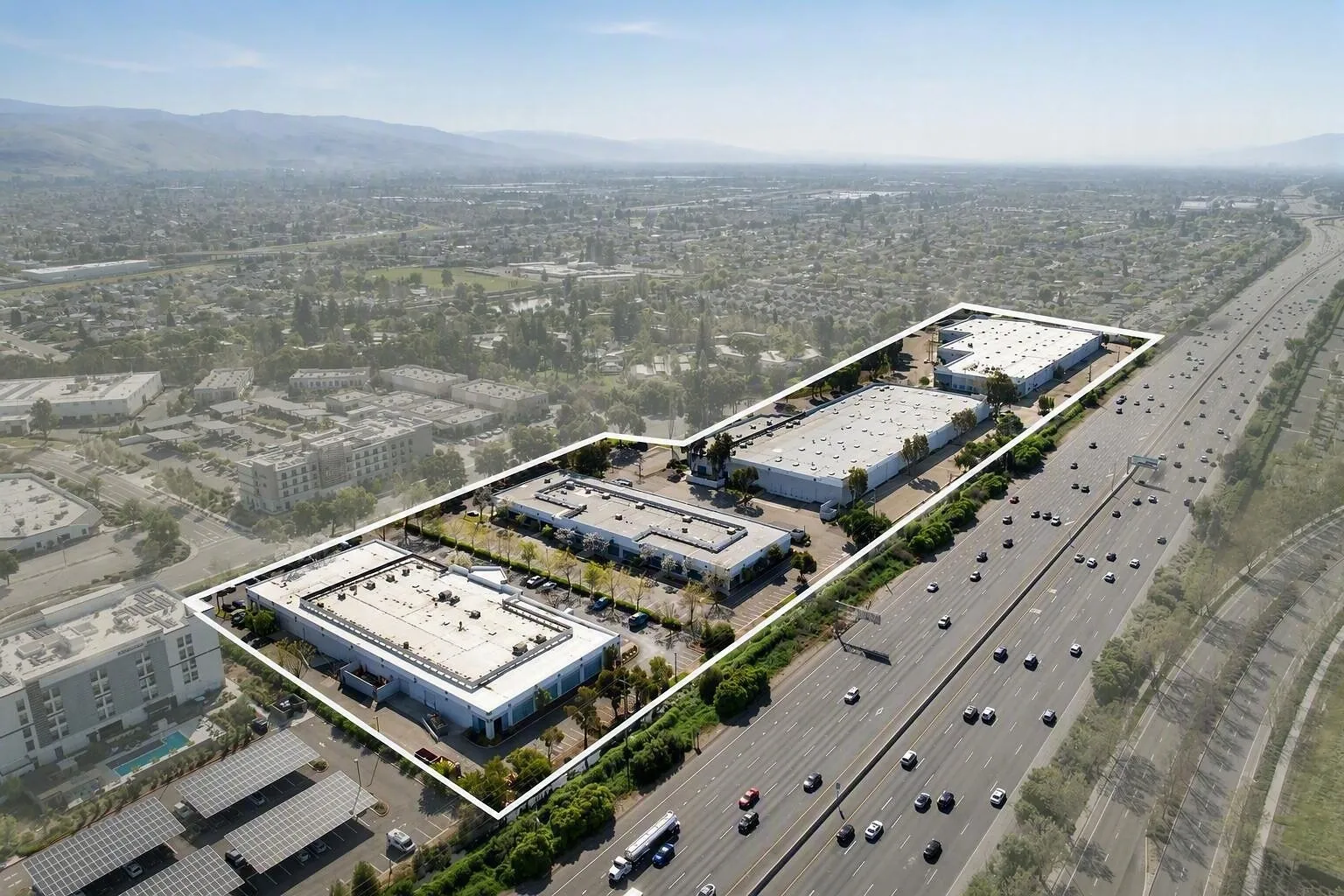 Aerial view of outlined industrial buildings beside a busy multi-lane freeway.