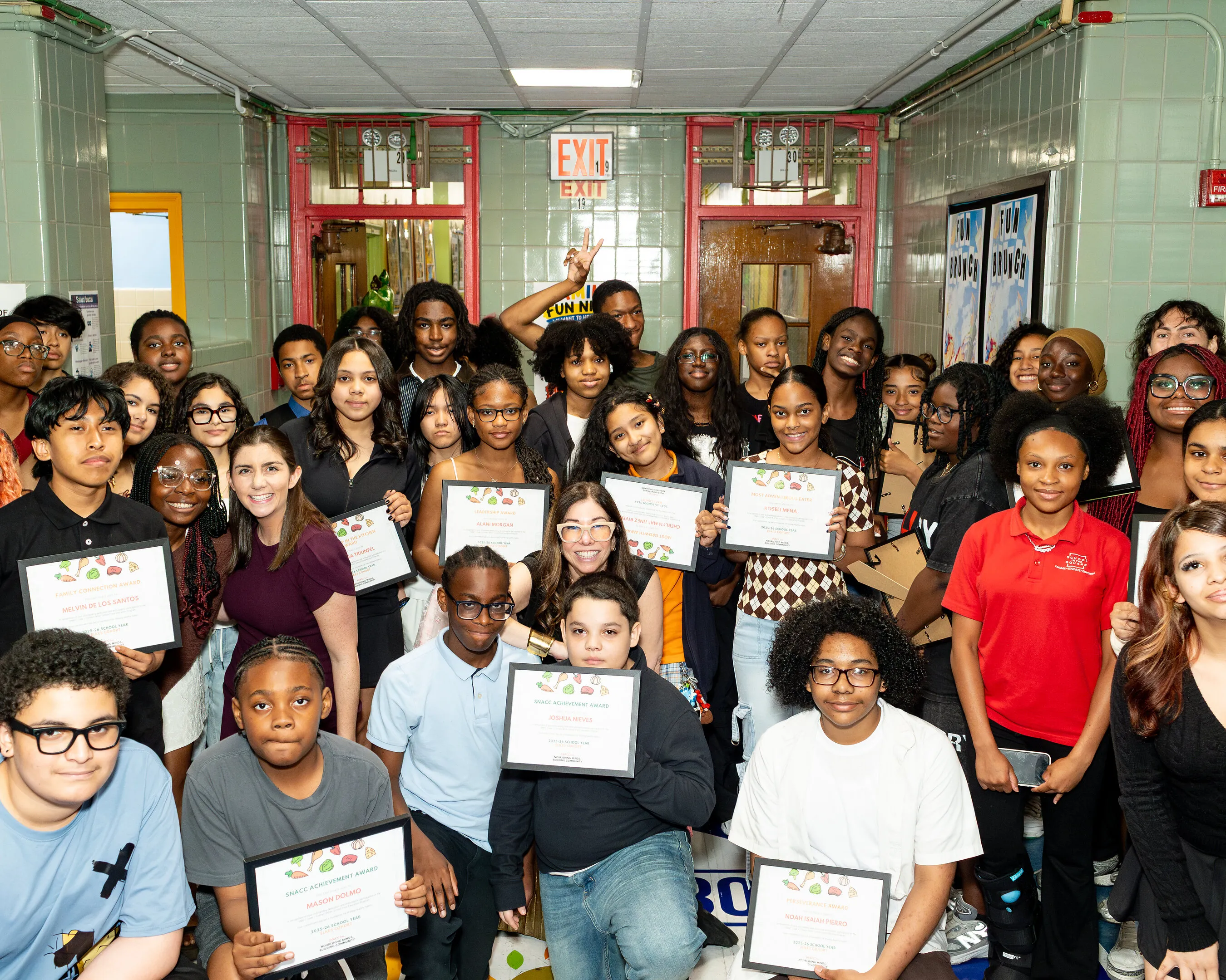 Students and staff pose together holding award certificates in a school hallway.