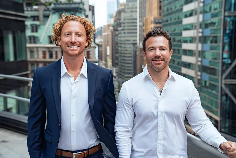 Two people in business attire standing on a city balcony with skyscrapers behind them