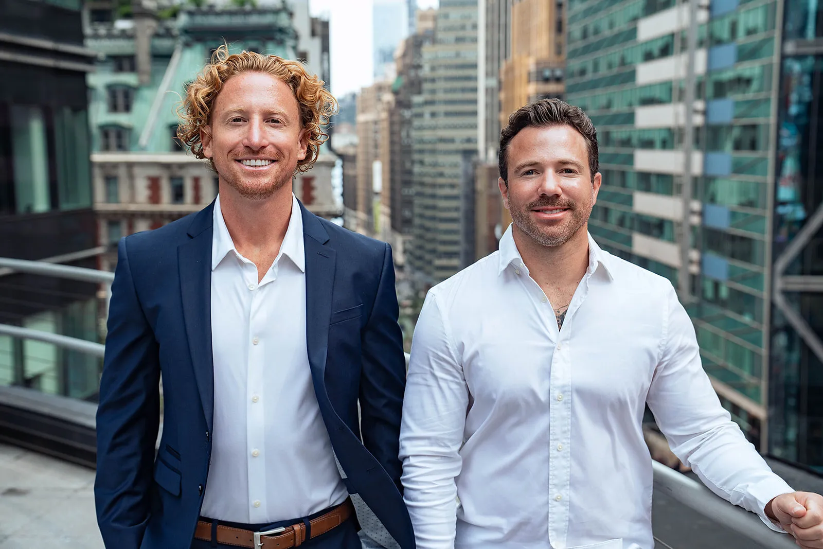Two people in business attire standing on a city balcony with skyscrapers behind them
