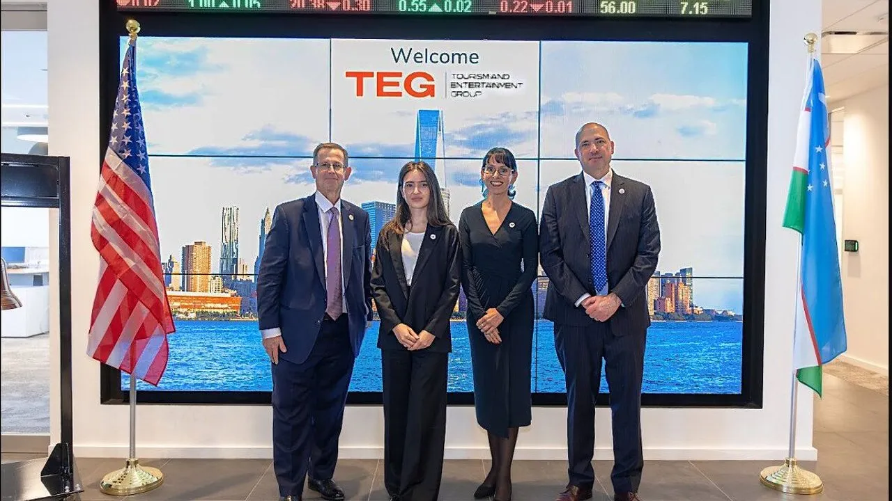 Four people in business attire stand between U.S. and Uzbekistan flags before a TEG display.