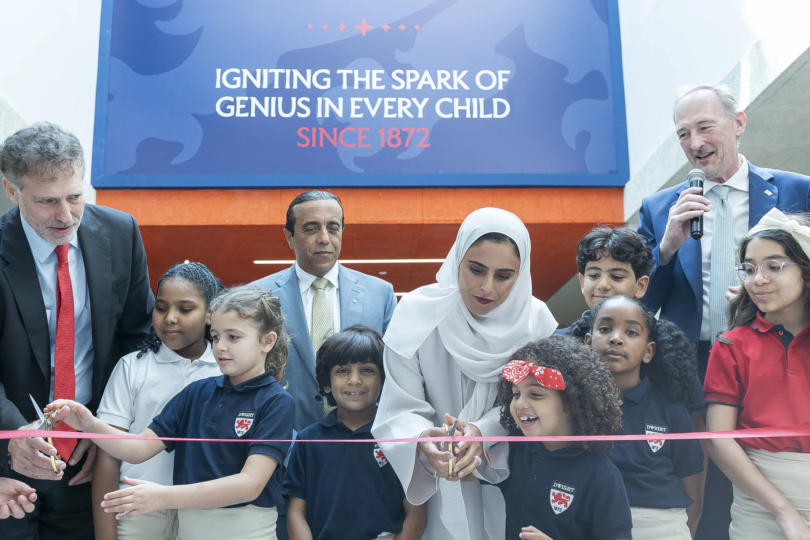 Adults and children cut a pink ribbon beneath a school sign.