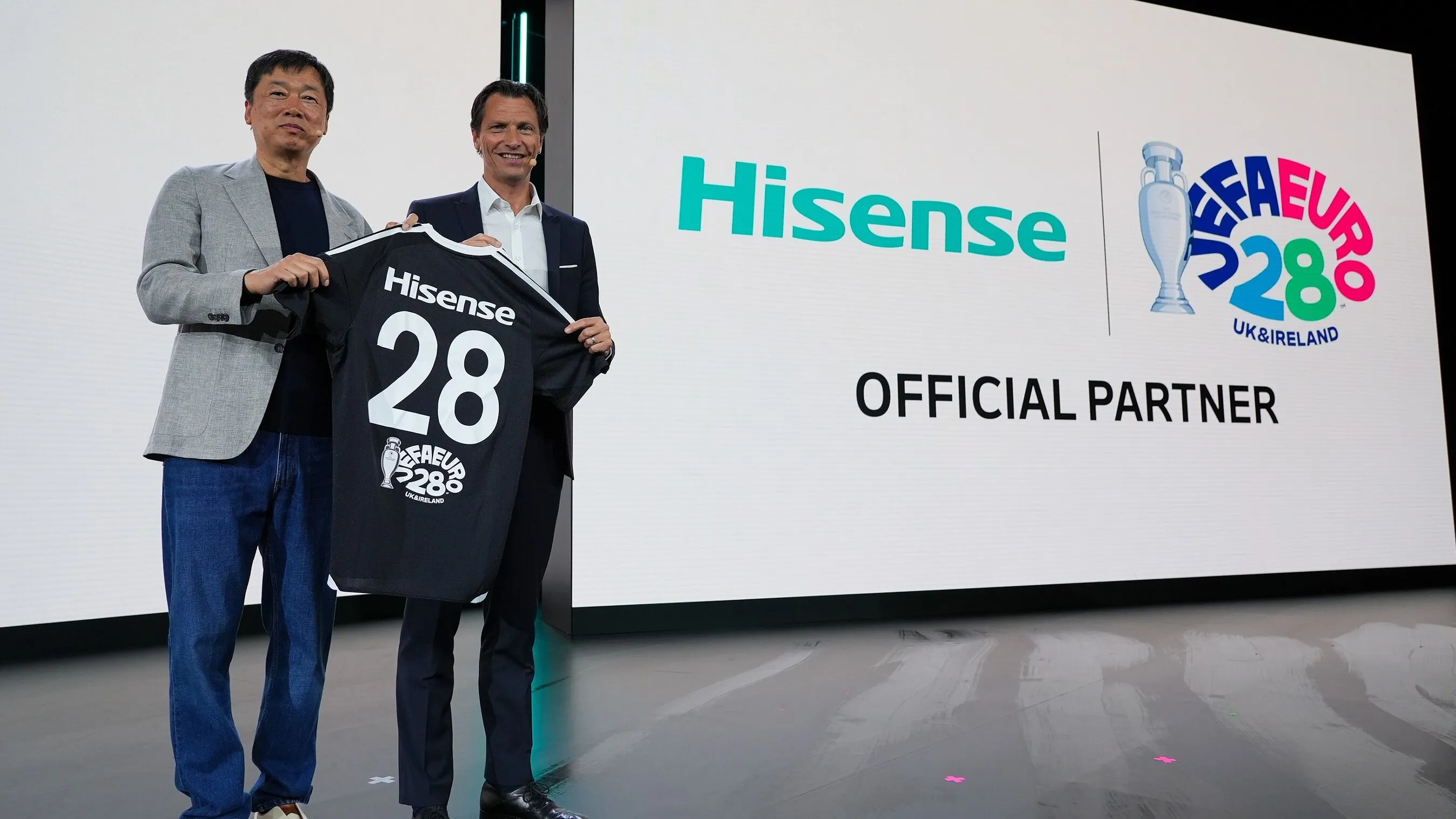 Two men hold a Hisense number 28 jersey beside a screen announcing UEFA Euro 2028 official partnership.