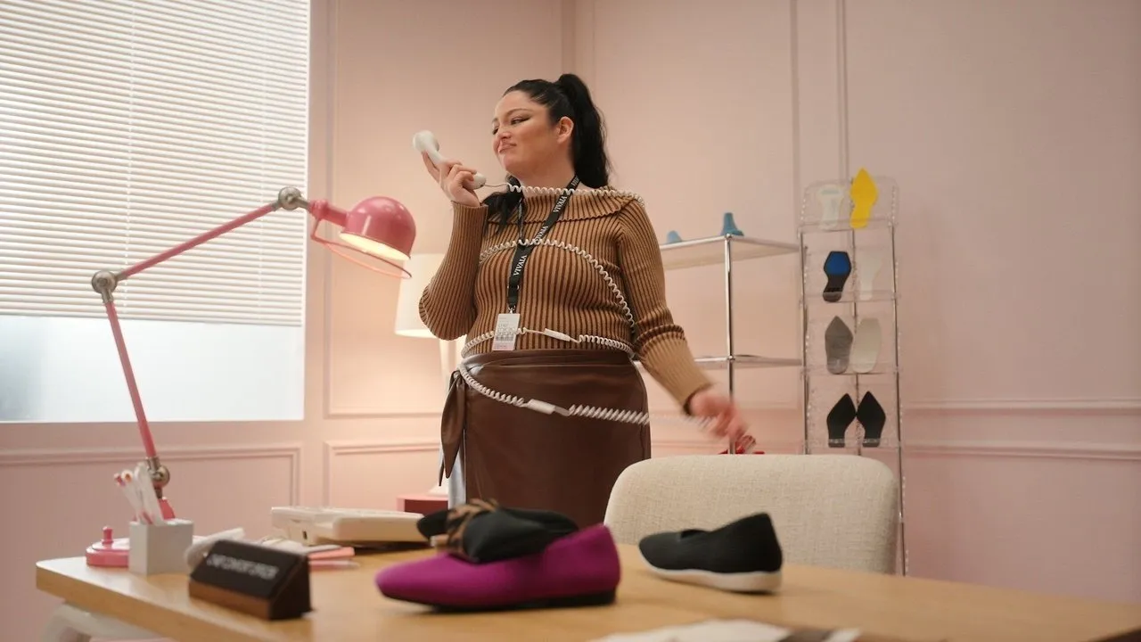 Woman on a corded phone in an office with shoes displayed on a desk and shelf