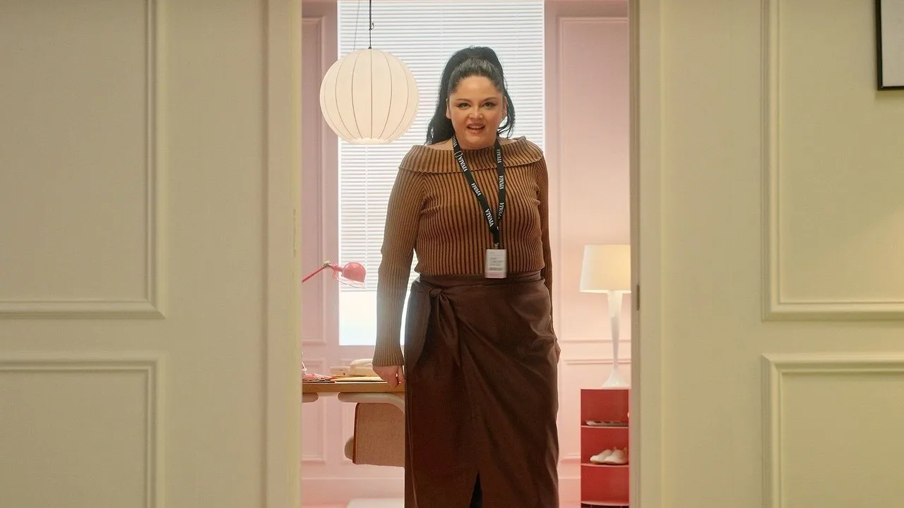 Woman wearing a brown sweater and skirt stands in an office doorway with a VIVAIA lanyard.