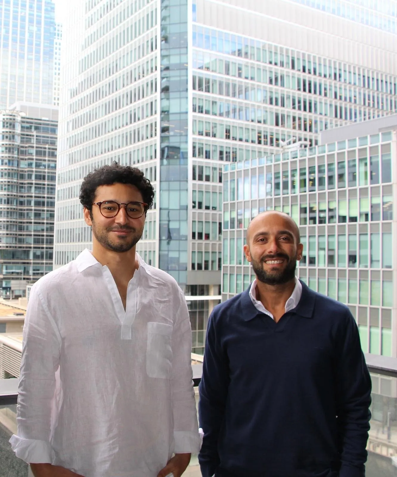 Two men standing in front of glass office towers.