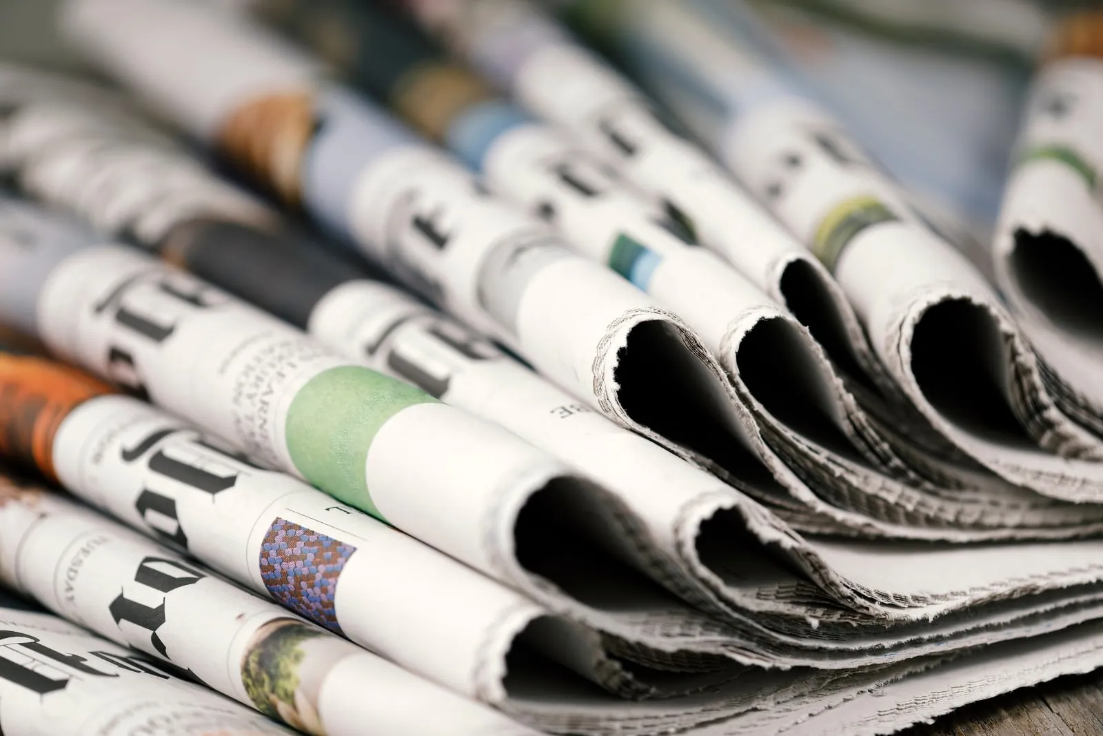 Folded newspapers lie piled together, their headlines in close view.