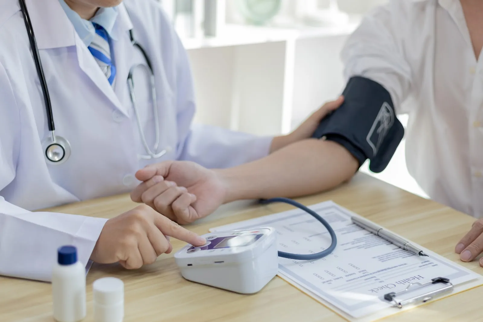 A doctor in a white coat fits a blood pressure cuff on a patient's arm and presses a button on the monitor.