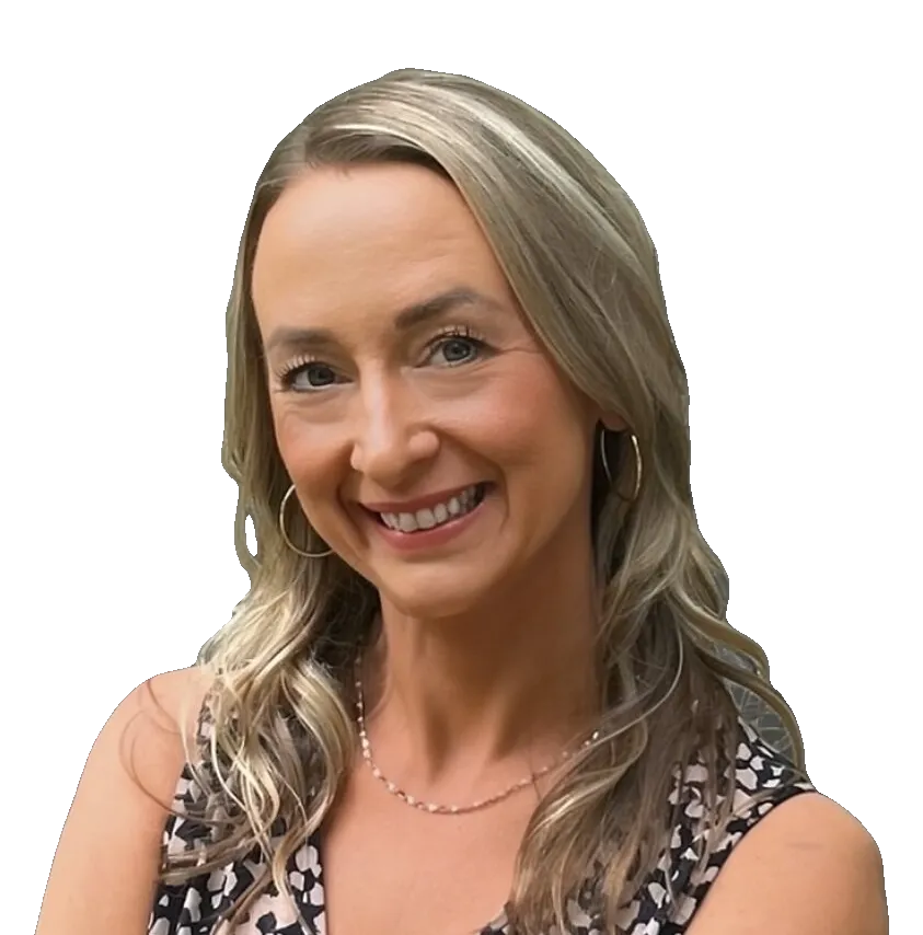 Kim Sizemore smiling with arms crossed, wearing a patterned sleeveless dress against a gray background.