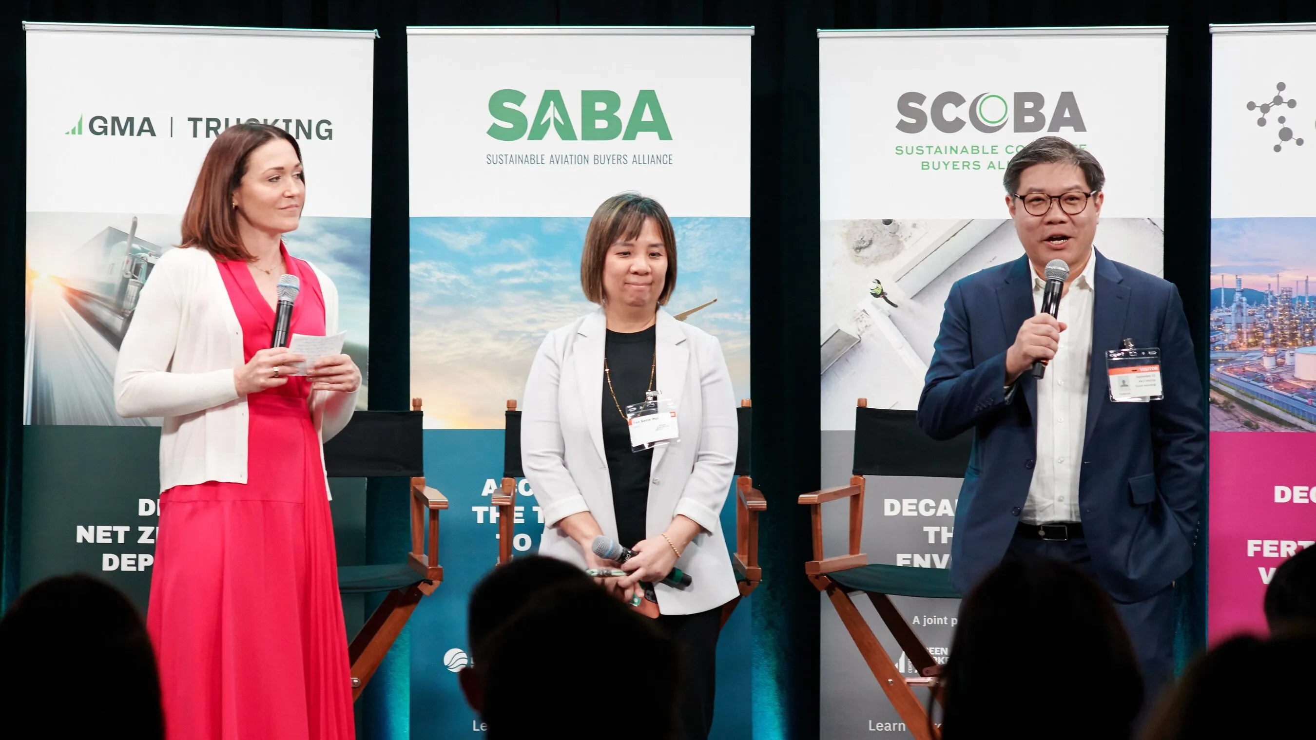 Three speakers with microphones stand before sustainable aviation alliance banners.
