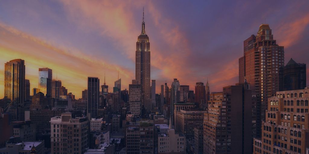 The Empire State Building rising above the Manhattan skyline at sunset, under a purple and orange sky