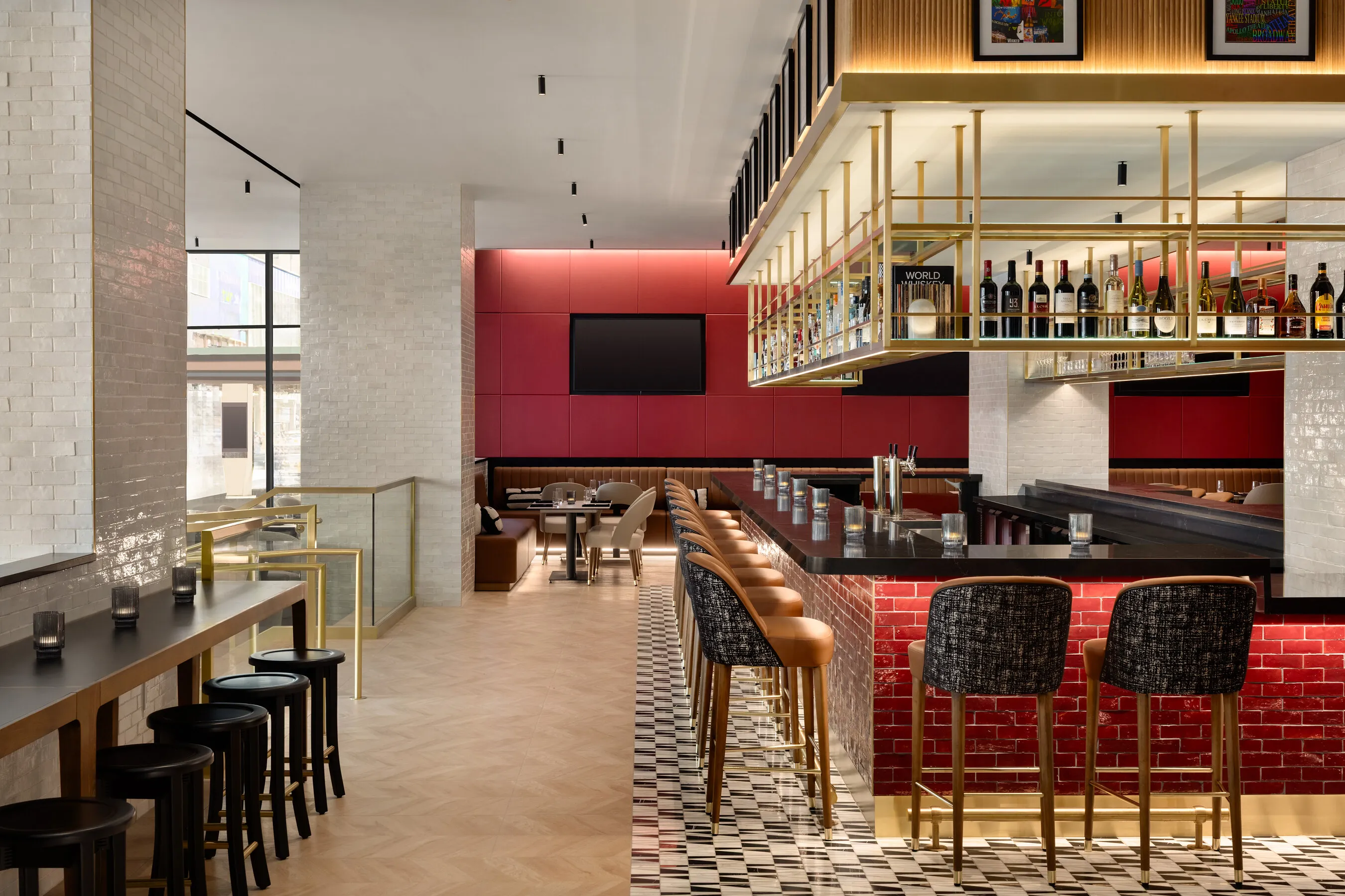 Modern restaurant bar with red tile, leather stools, dining tables and overhead shelves of liquor bottles.