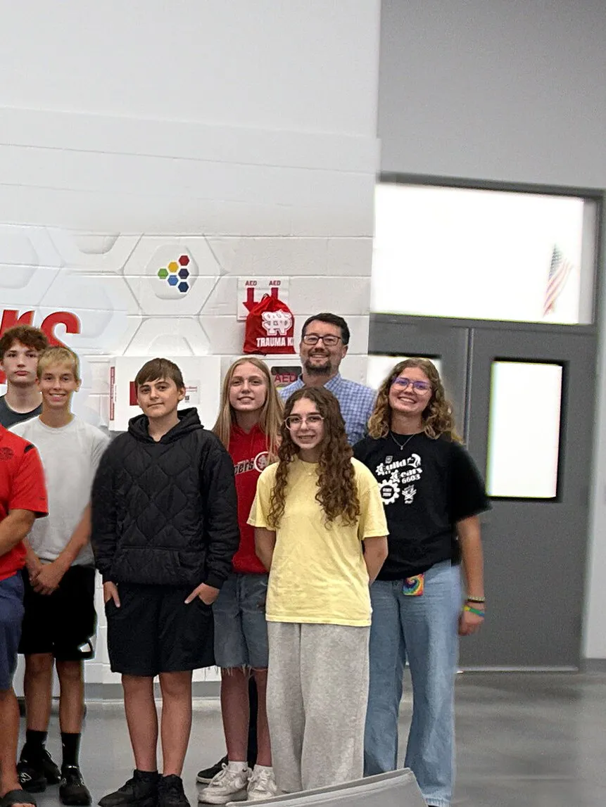 A group of students and adults hold a large check and signed banner in a school hallway.