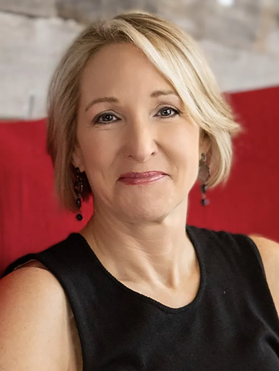 Laurie Pasler wearing a black sleeveless top and dangling earrings against a red background.