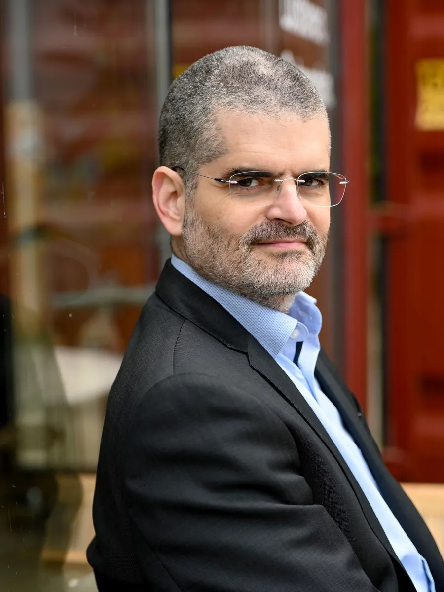 Bernardo Kastrup in glasses, a dark suit jacket and blue shirt, seated beside a window.
