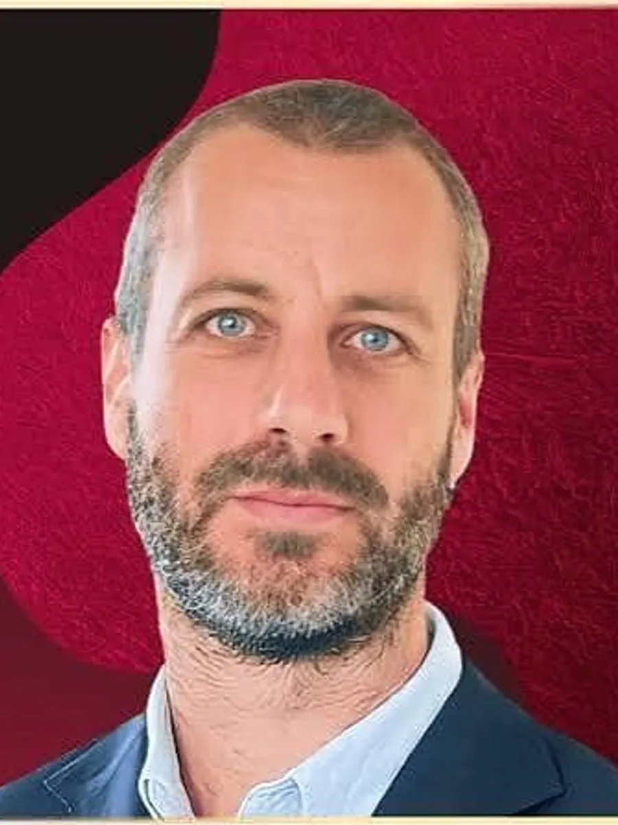 Blake Hutchison in a navy jacket and light blue shirt against a red background.