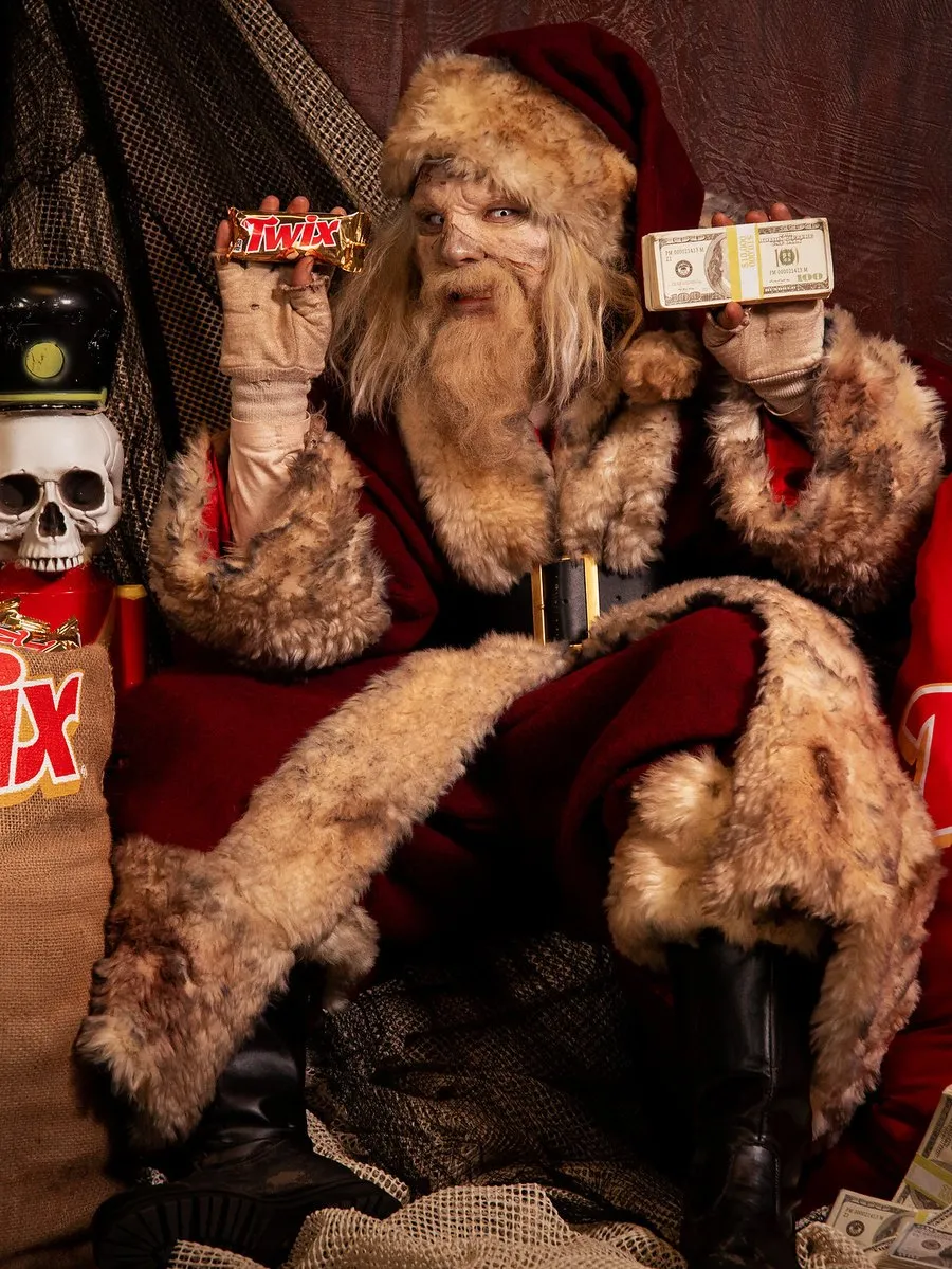 A Santa-like figure holds Twix bars and cash beside Halloween decorations and Twix sacks.