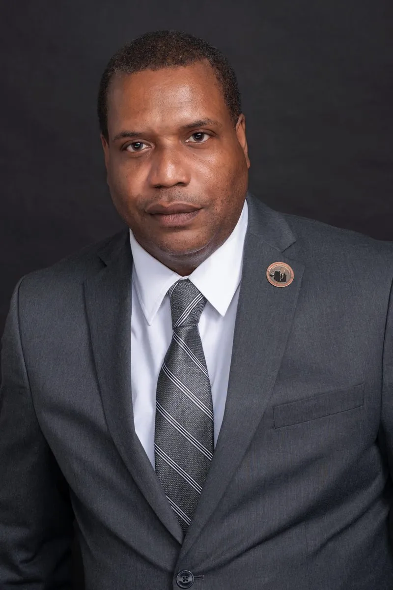 Phil Andrews, founding president of the New York City Minority Small Business Chamber of Commerce, in a gray suit and striped tie against a dark backdrop.