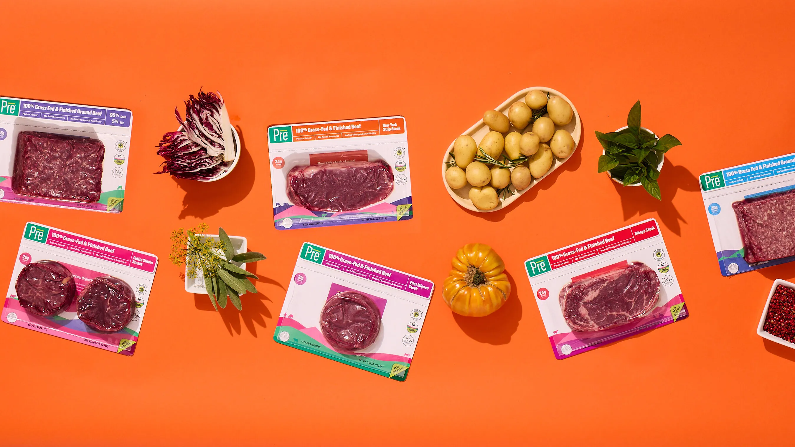 Packaged beef cuts with potatoes, radicchio, herbs, squash and peppercorns on an orange background.